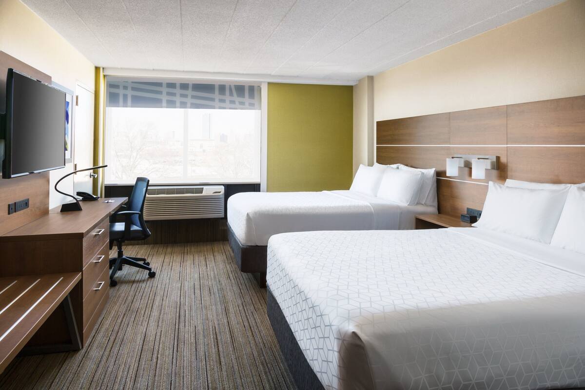 Hotelkamer met twee bedden, een bureau, een stoel, een televisie en een raam met uitzicht op de stad.