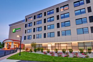 Een modern hotelgebouw met een opvallend 'Holiday Inn Express' bord, meerdere ramen en een goed onderhouden tuin met bloemen.
