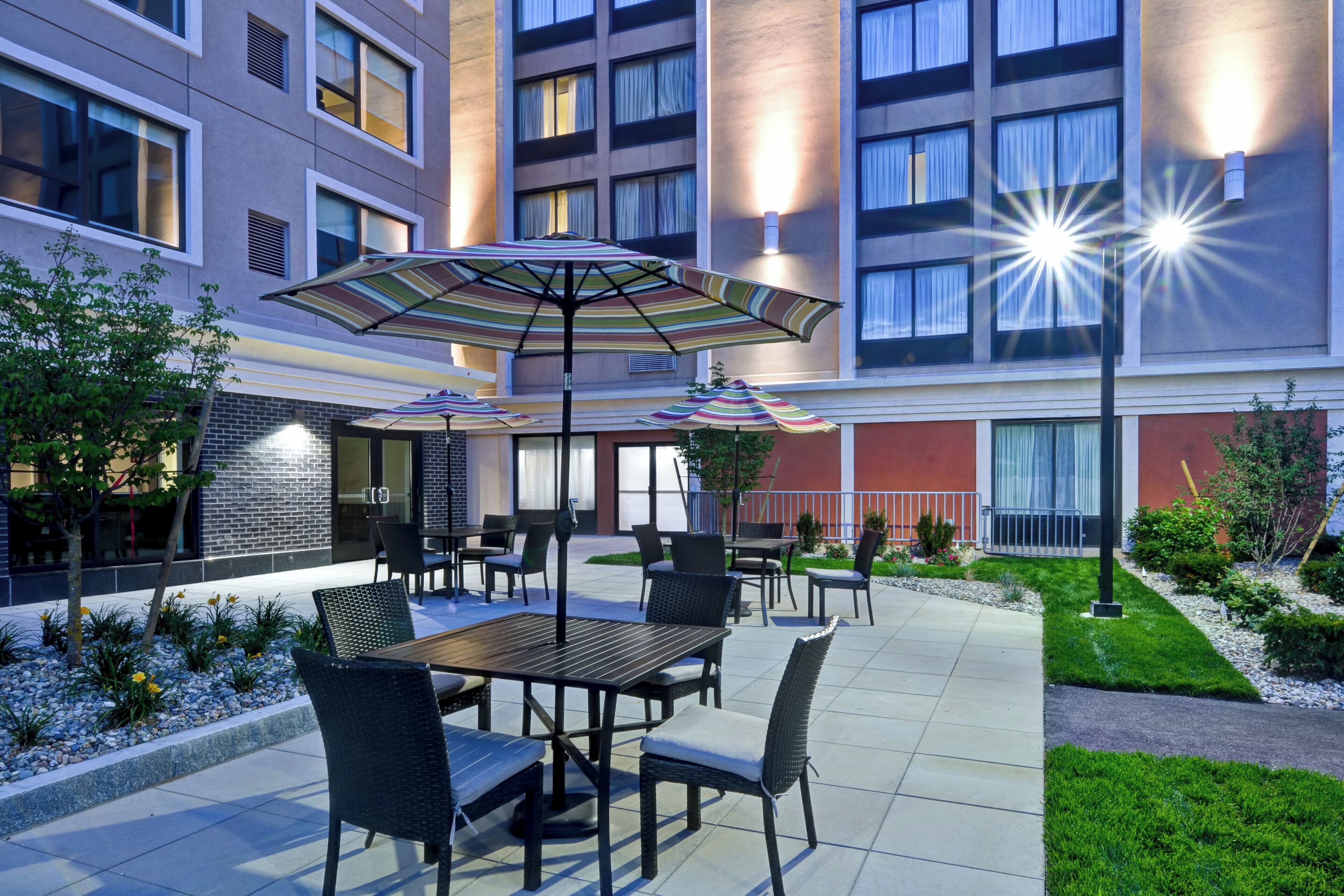 Un espace extérieur aménagé en terrasse, avec des tables et des chaises, des parasols et un jardin bien entretenu.