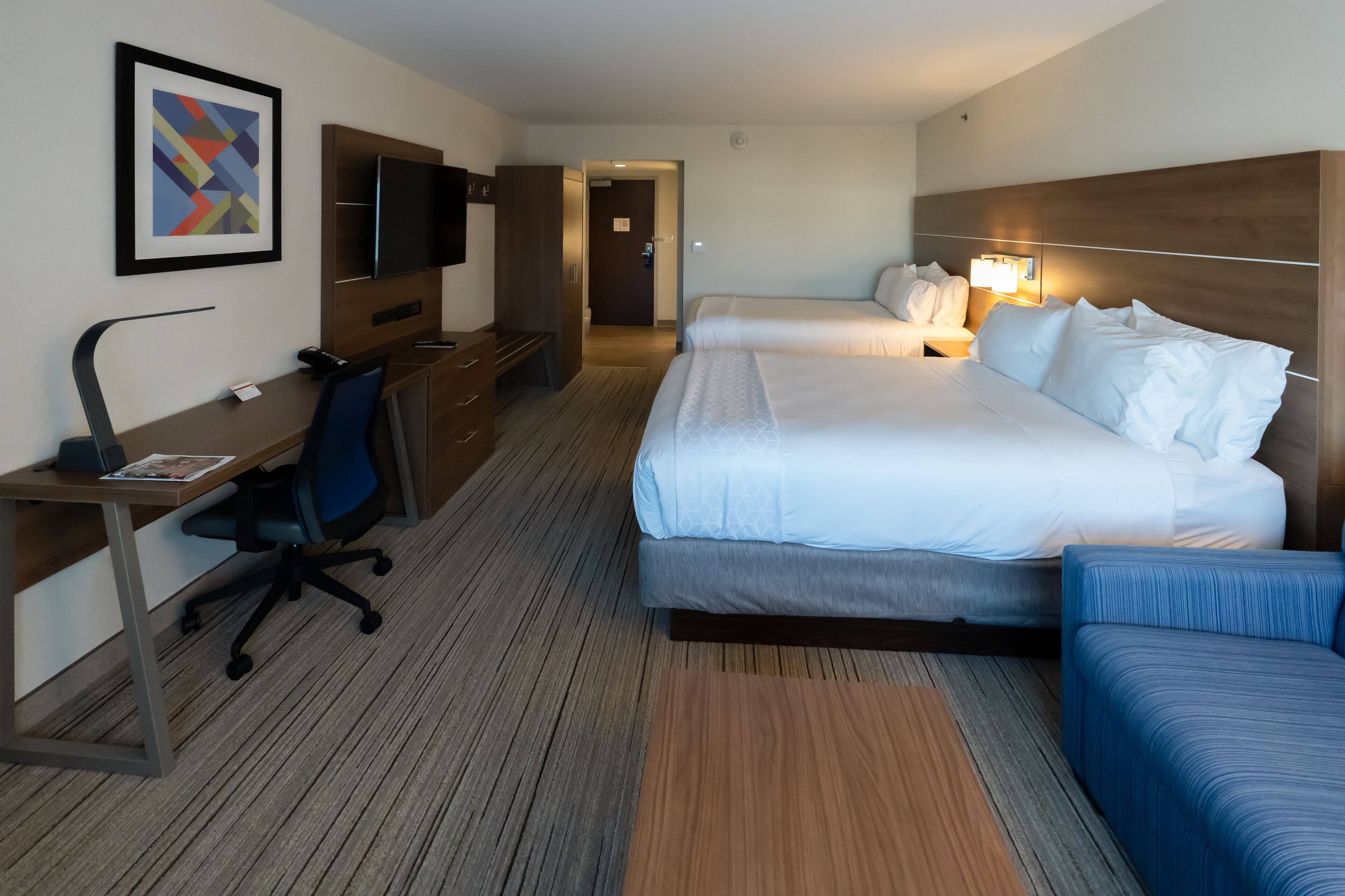 Habitación de hotel con cama, escritorio con silla, televisión y un cuadro en la pared.