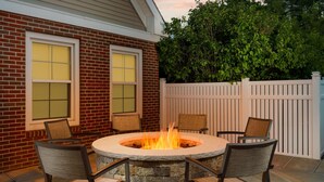 A patio with a stone fire pit surrounded by four chairs, a brick wall, and a white fence. - Residence Inn by Marriott Foxborough (Foxborough)