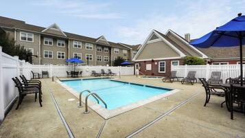 A rectangular swimming pool with a white deck, surrounded by lounge chairs and umbrellas.