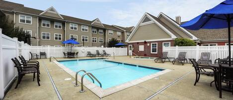 A rectangular swimming pool with a white deck, surrounded by lounge chairs and umbrellas.