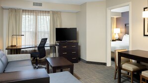 A hotel room with a flat-screen TV, a desk with a chair, a sofa, a small table, and a bed with a nightstand. - Residence Inn by Marriott Foxborough (Foxborough)