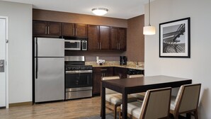 A modern kitchen with stainless steel appliances, dark wooden cabinets, and a dining area with a table and chairs. - Residence Inn by Marriott Foxborough (Foxborough)
