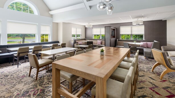A spacious room with a large wooden table, multiple seating arrangements, and large windows offering a view of the outdoors. - Residence Inn by Marriott Foxborough (Foxborough)