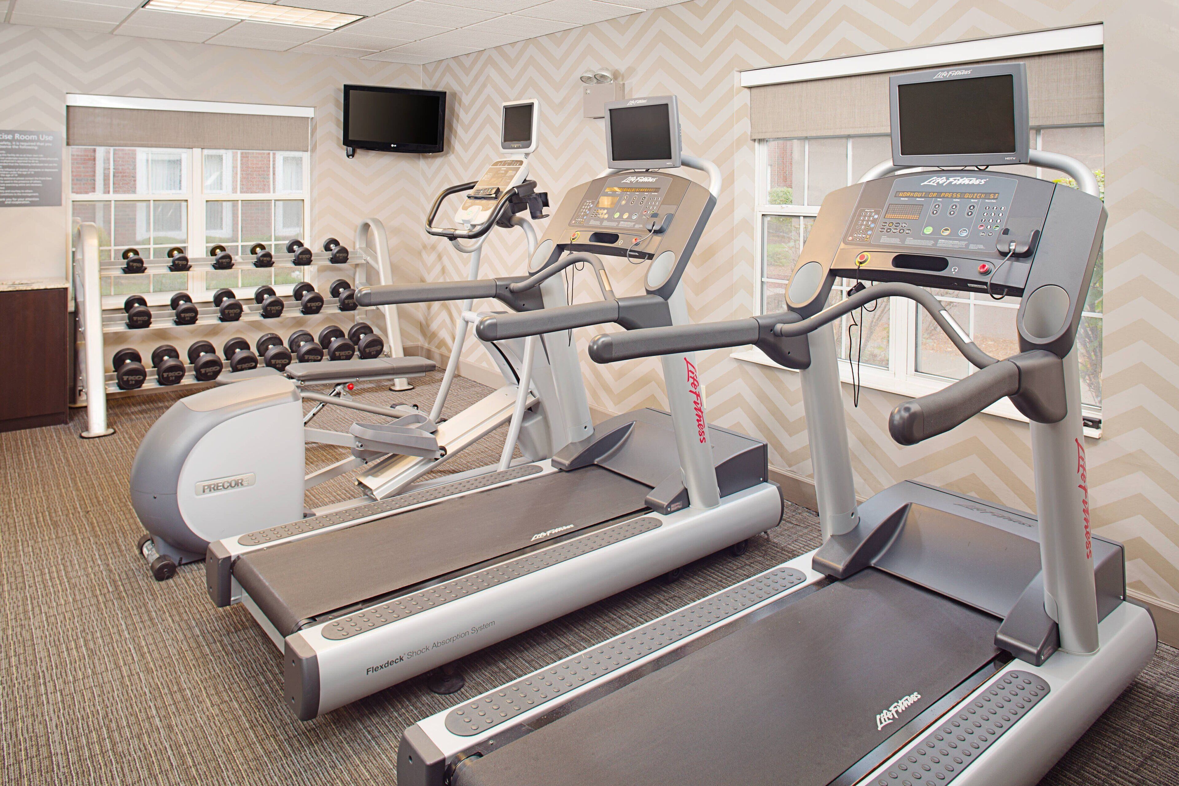 A fitness center with treadmills, elliptical machines, and a wall of dumbbells.
