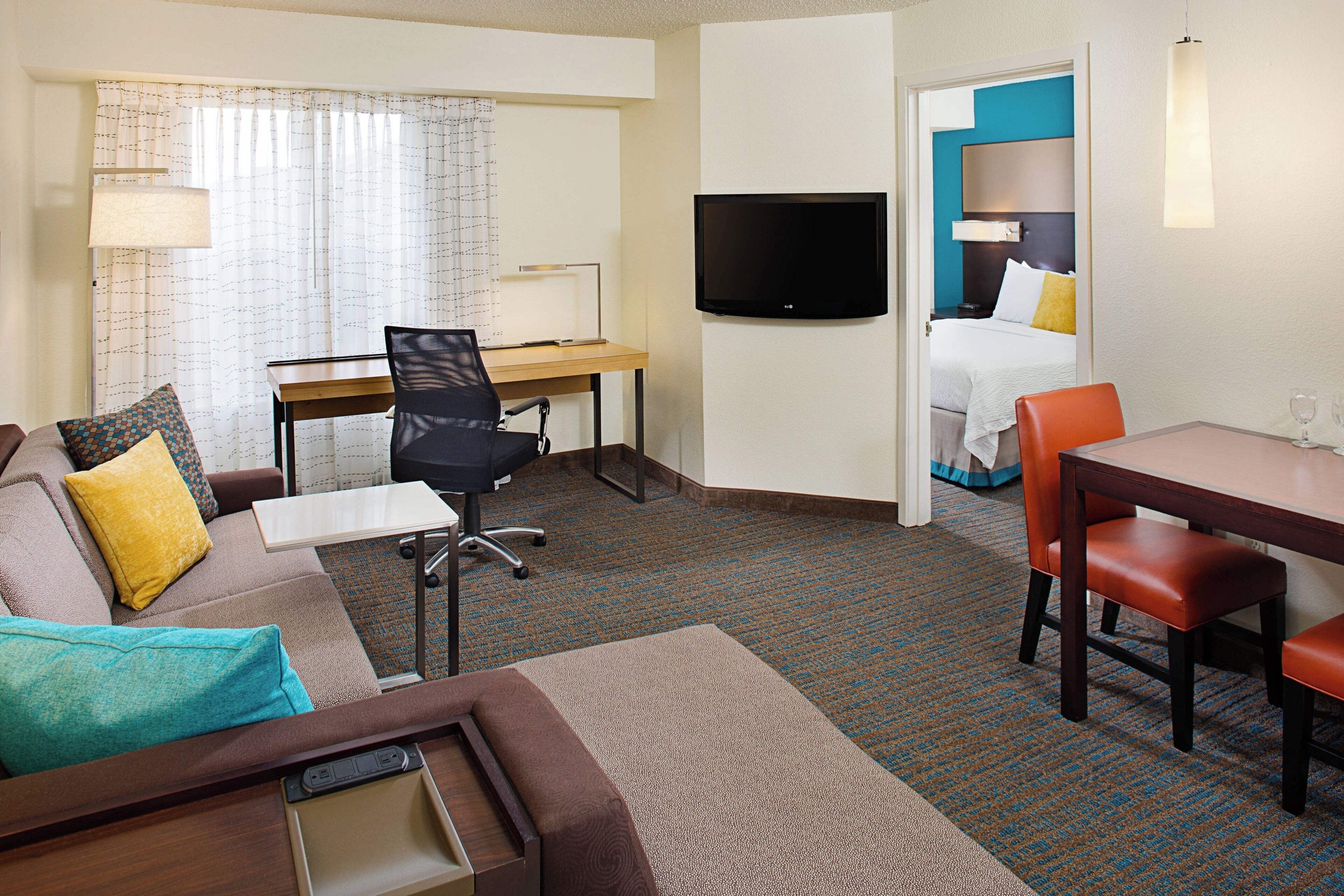 A hotel room with a sofa, a desk, a TV, a dining table, and a bed.