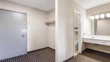 A hotel bathroom with a white door, a mirror with lights, a sink, and a toilet.