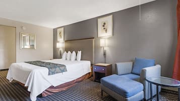 A hotel room with a bed, a chair, a small table, and two wall-mounted lamps.