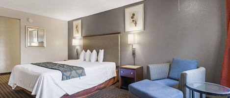 A hotel room with a bed, a chair, a small table, and two wall-mounted lamps.
