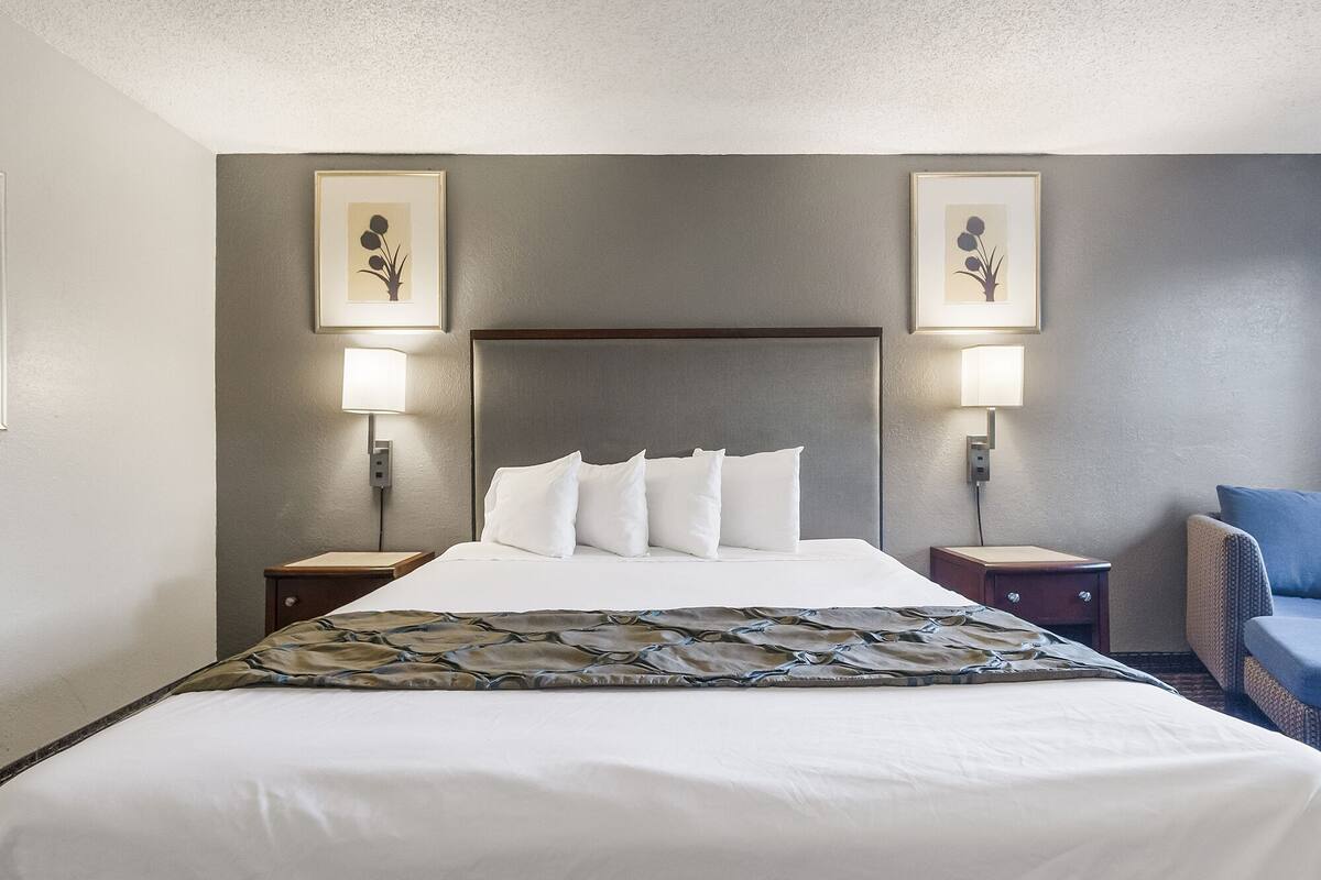 Habitación de hotel con una cama grande, dos mesitas de noche, un cabecero y dos lámparas fijadas a la pared.