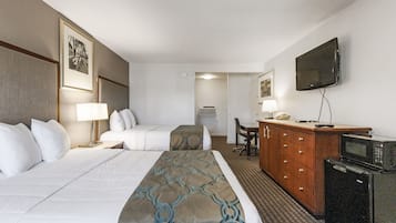 A hotel room with two beds, a desk, a dresser, a television, and an air conditioning unit.