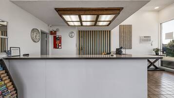 Zona de recepción con mostrador de check-in, un reloj, detector de incendios y ventana con vistas al exterior.