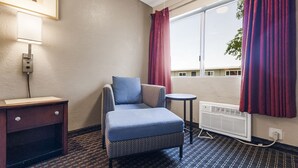 Une chambre d’hôtel avec un canapé, une petite table ronde, un radiateur et une fenêtre avec des rideaux.