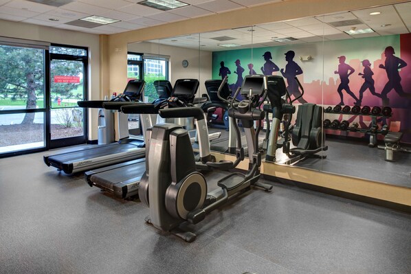 A gym with treadmills, ellipticals, and a wall mural of runners.