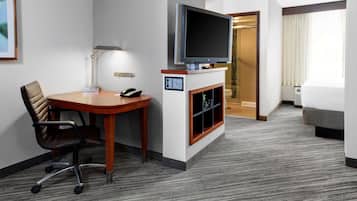 A hotel room with a flat-screen TV, a desk with a chair, a fireplace, a bed, and a staircase leading to another room.