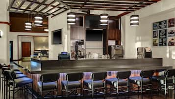 A modern bar area with a long counter, multiple bar stools, and overhead lighting.