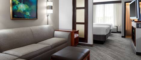 A hotel room with a sofa, a small table, a bed, a TV, and a painting on the wall.