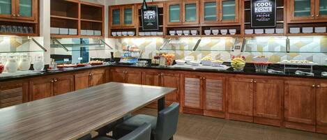 A modern kitchen with wooden cabinets, a long dining table, and a glass display case.