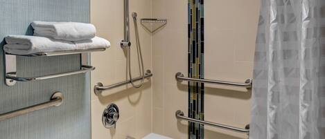 Un baño con bañera, ducha con cabezal de ducha manual y toallero con toallas dobladas.