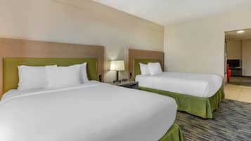 A hotel room with two beds, a nightstand, a lamp, and a television in the corner.