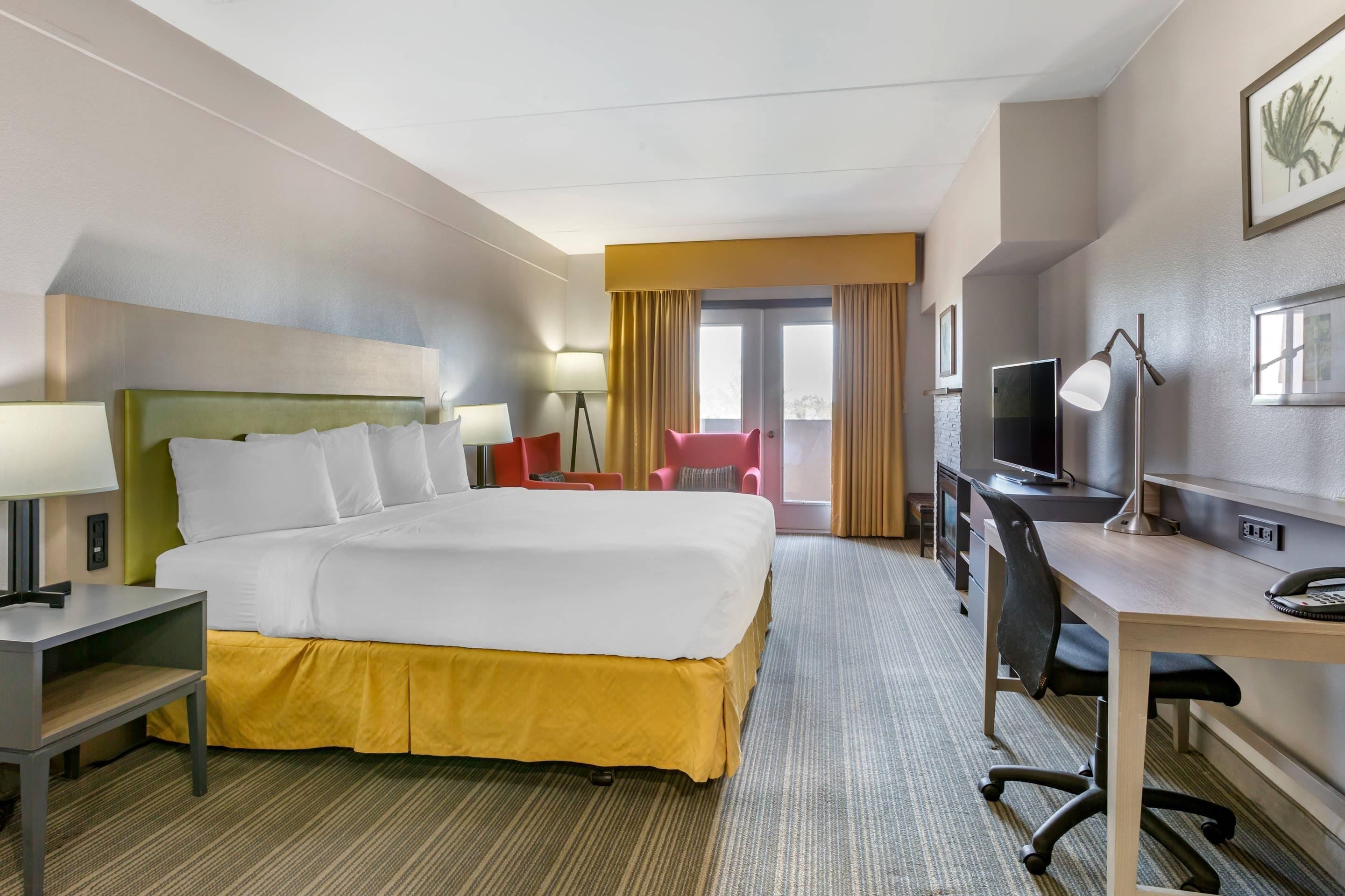 Habitación de hotel con cama, escritorio, silla, televisor y ventana con cortinas.