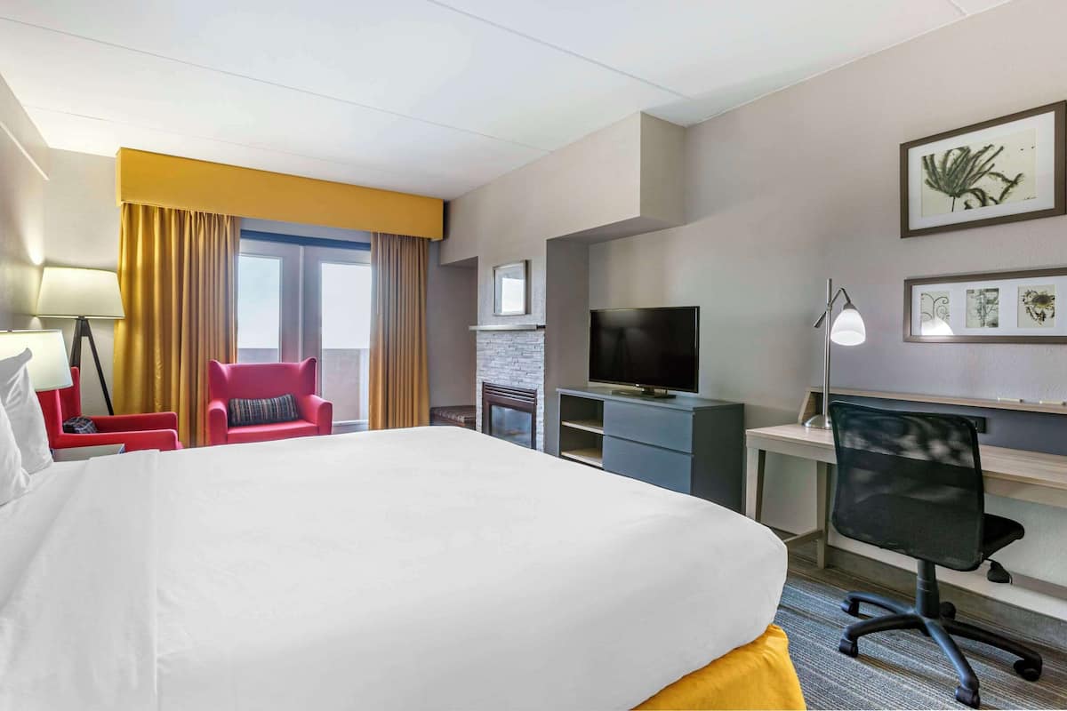 A hotel room with a large bed, a desk with a computer, a TV, and a red chair.
