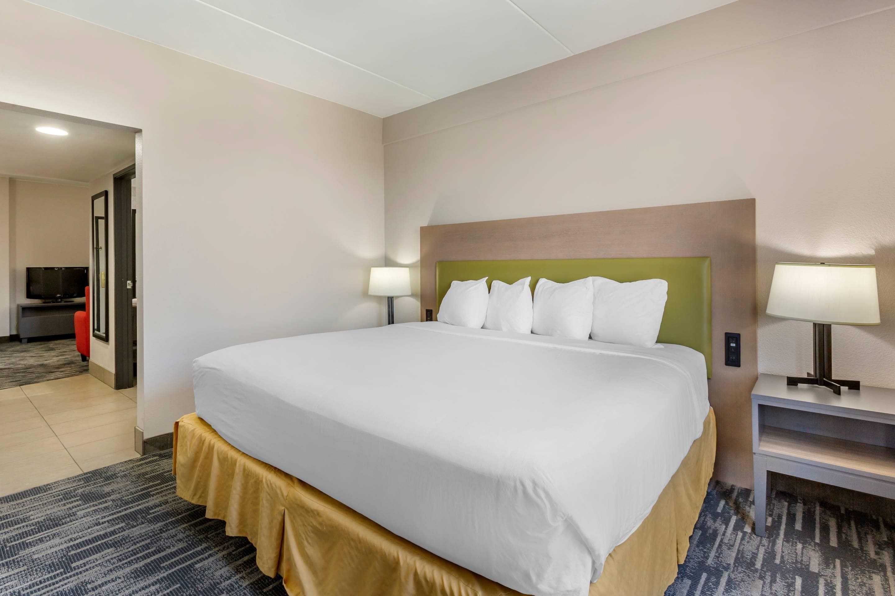 A hotel room with a large bed, two bedside lamps, a television, and a desk with a lamp.