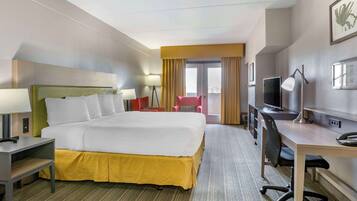 A hotel room with a large bed, a desk with a computer, a TV, and a chair.