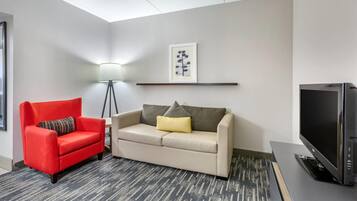 A modern living room with a red armchair, a beige sofa, a floor lamp, a framed picture on the wall, and a flat-screen TV.