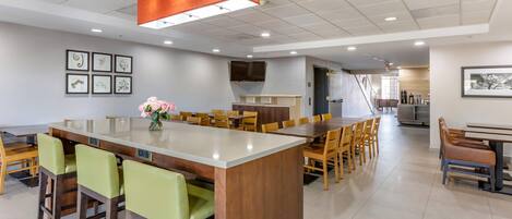 A modern dining area with a central island, multiple seating options, and a flat-screen TV mounted on the wall.