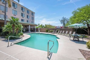 A hotel pool area with a clear pool, lounge chairs, and a building in the background.
