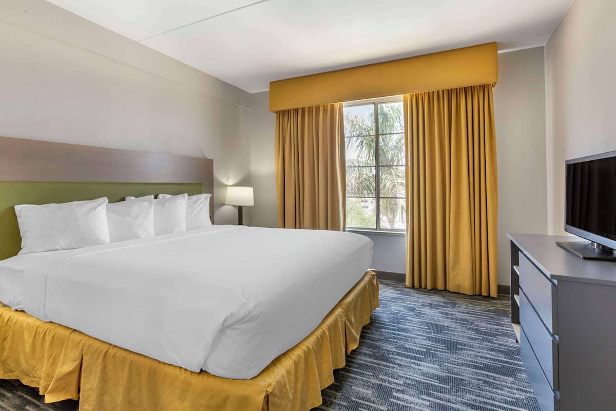 A hotel room with a large bed, a television, a desk, and a window with curtains.