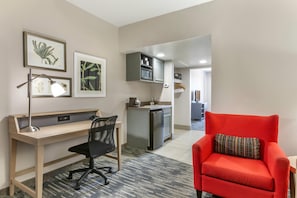 A compact hotel room with a desk, chair, kitchenette, and a red armchair. - Country Inn & Suites by Radisson, Mesa, AZ (Mesa)