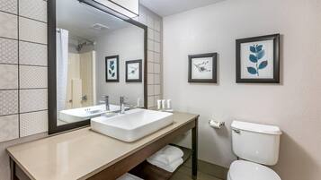Un baño moderno con un espejo grande, dos lavamanos, un inodoro y obras de arte enmarcadas en la pared.