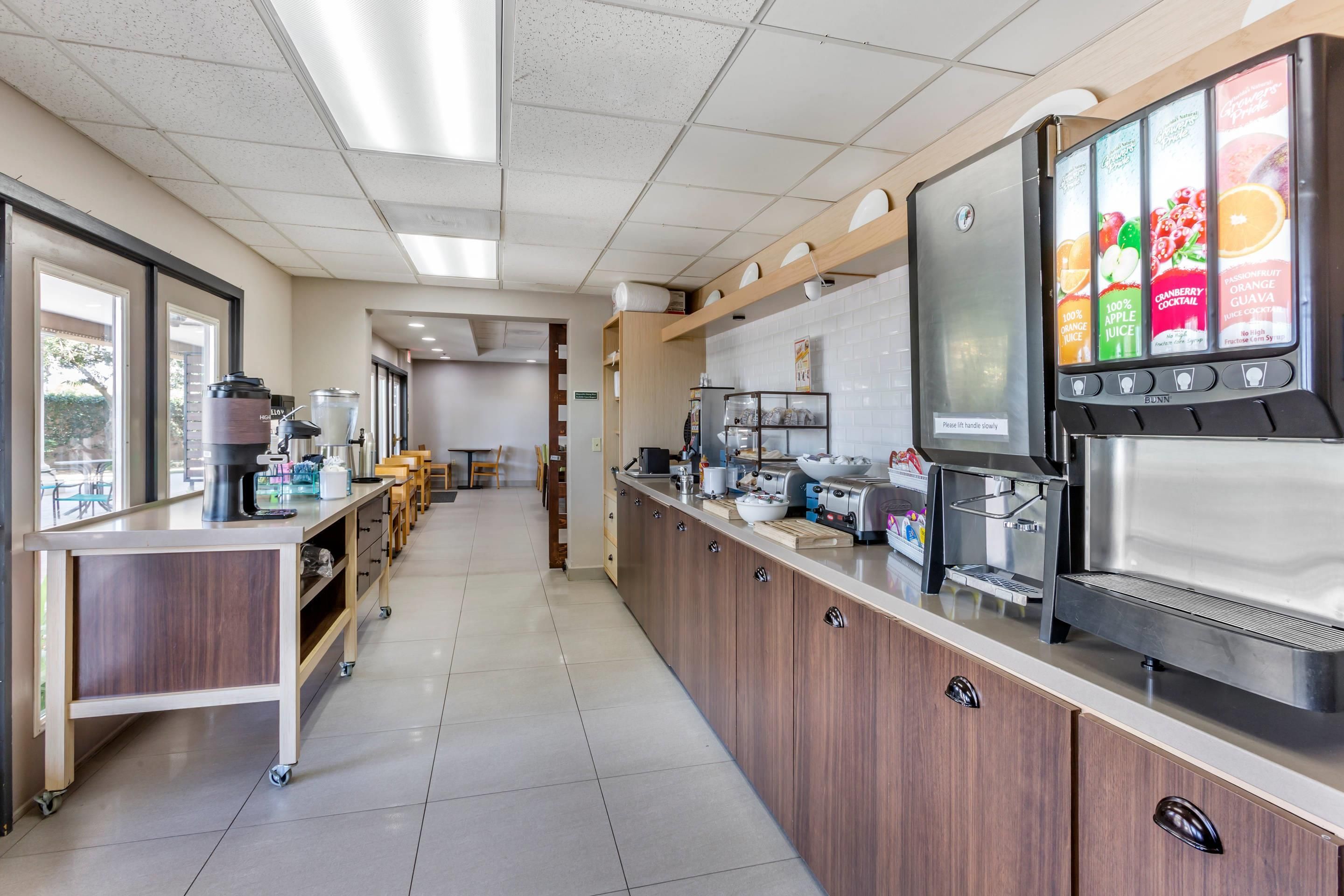 A commercial kitchen with a coffee machine, a beverage dispenser, and a counter with various items.
