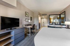 Une chambre d’hôtel équipée d’un téléviseur à écran plat, d’un bureau, d’une chaise, d’un lit, d’une salle de bain avec un miroir et d’une fenêtre.