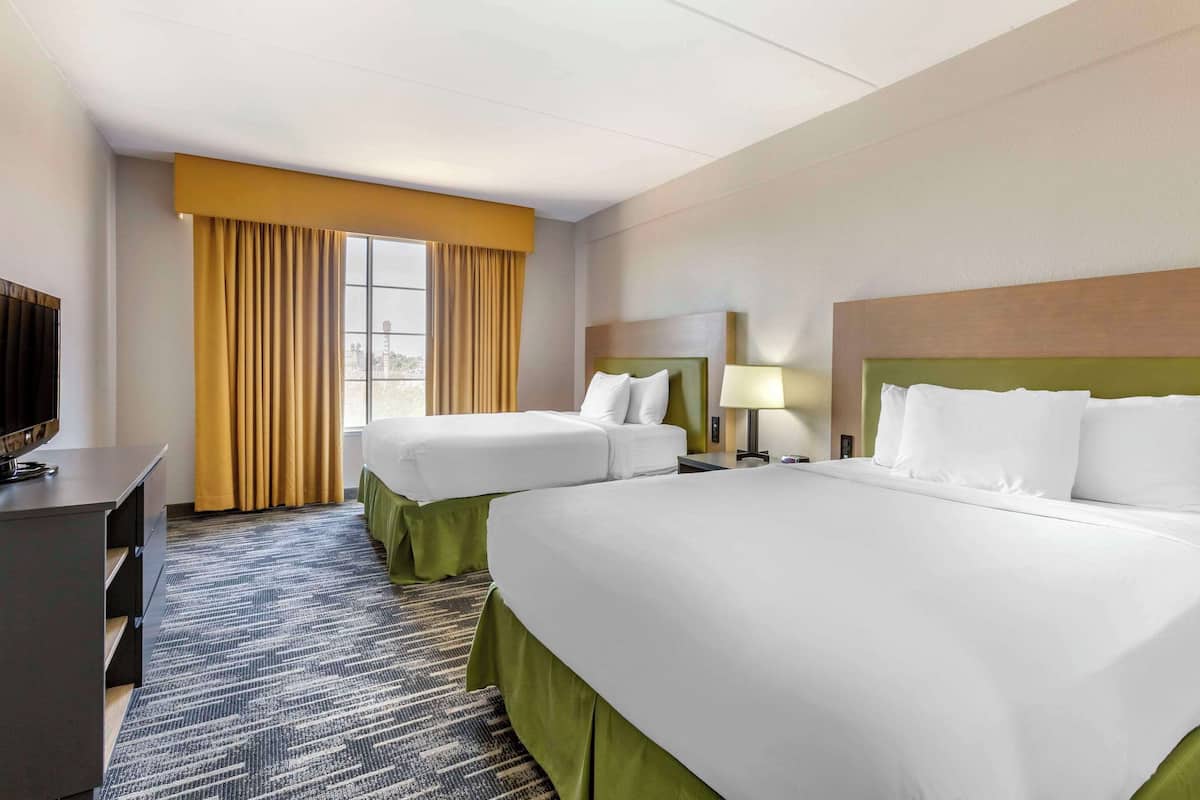 A hotel room with two beds, a desk, a TV, and a window with curtains.