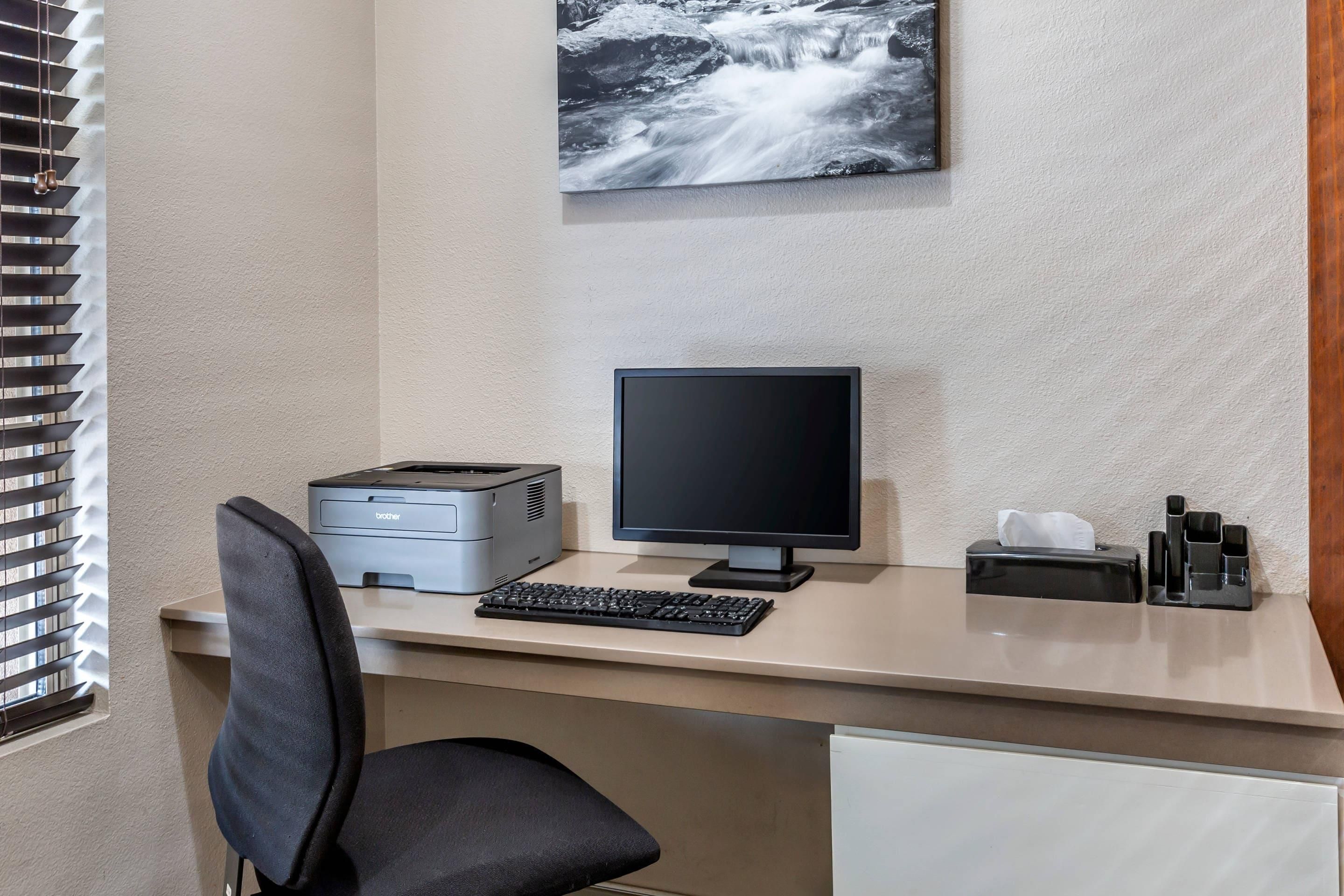 A hotel office desk with a computer, printer, keyboard, and a tissue box.