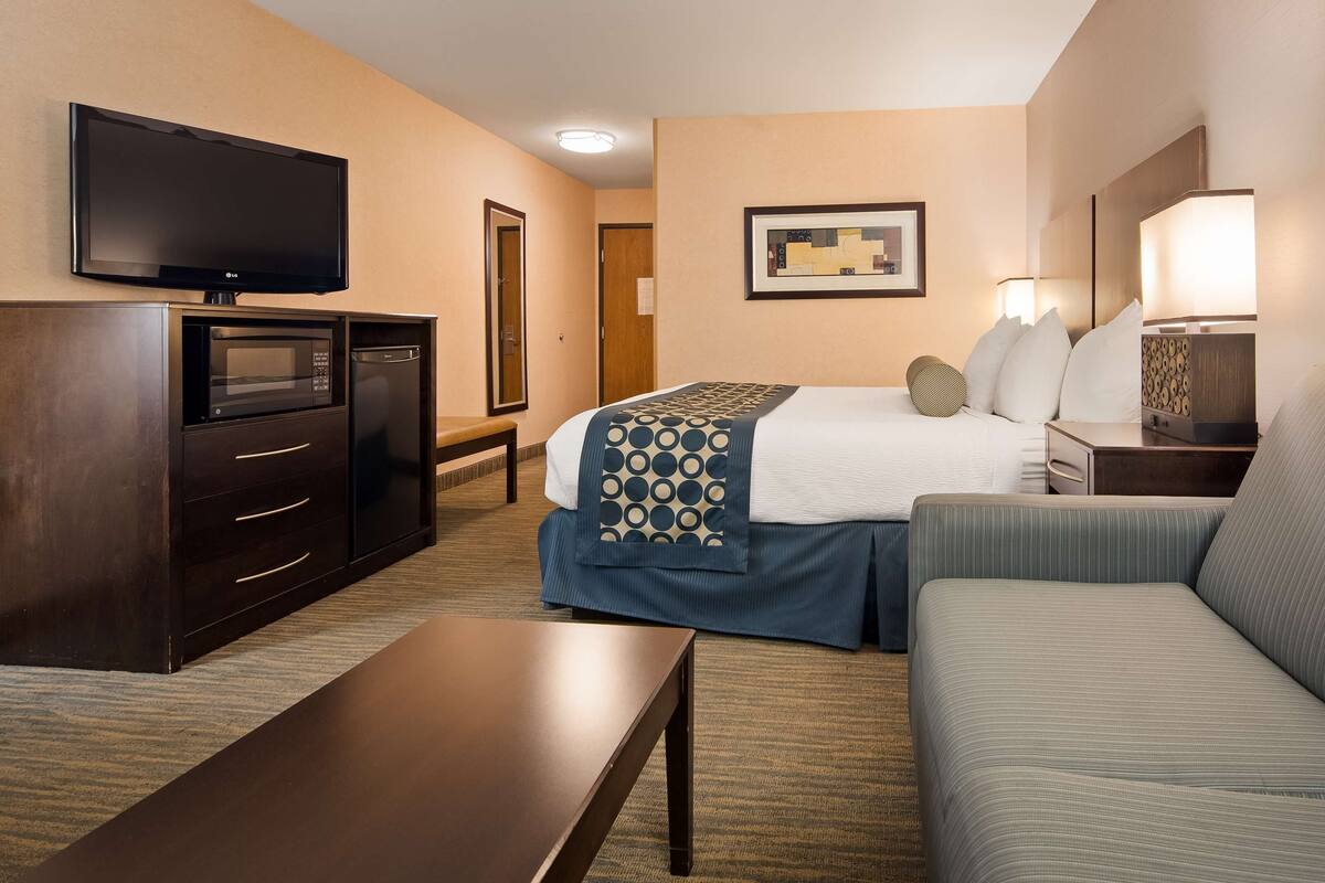 Habitación de hotel con cama, sofá, televisor, escritorio y lámpara.