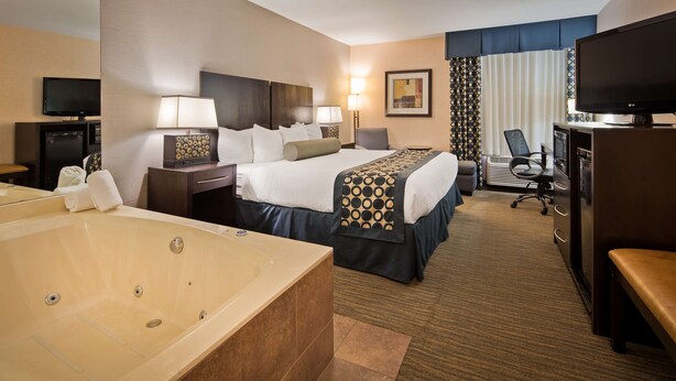 A hotel room with a large bathtub, a bed with a patterned bedspread, a desk with a computer, and a television. - Best Western Plus Coldwater Hotel (Coldwater)