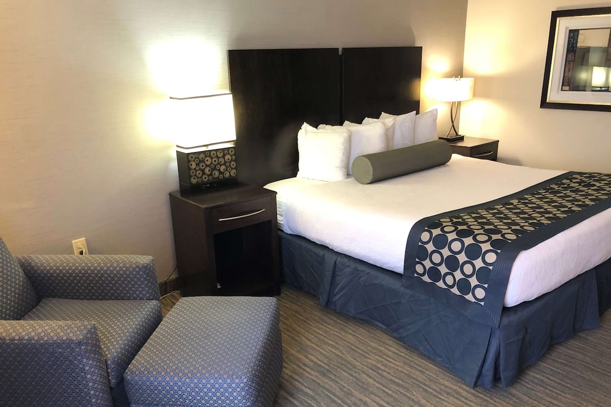 Habitación de hotel con una cama bien hecha, dos mesitas de noche con lámparas, una silla y suelo alfombrado.