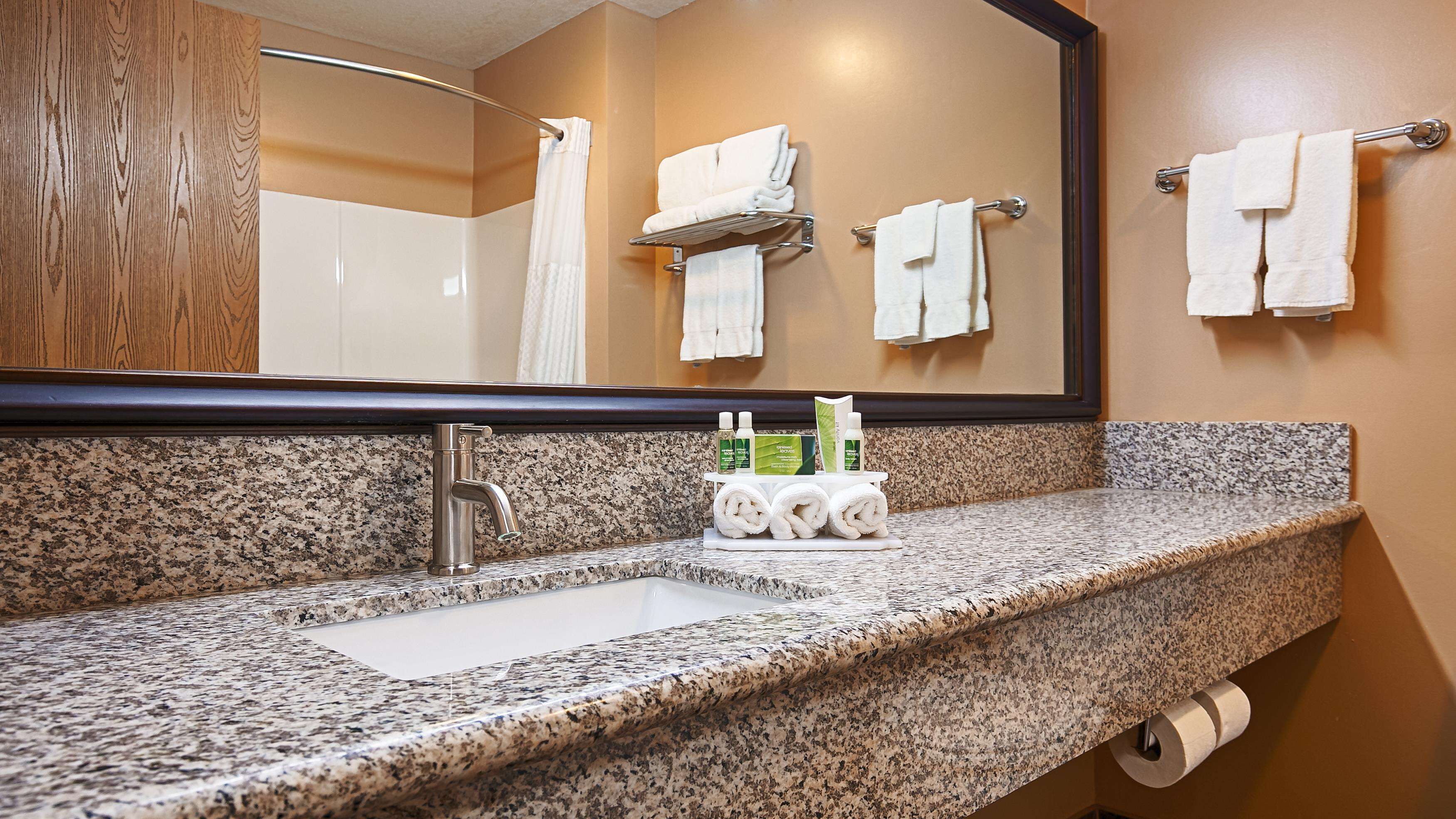 A bathroom with a granite countertop, a sink, a mirror, and a towel rack with folded towels.