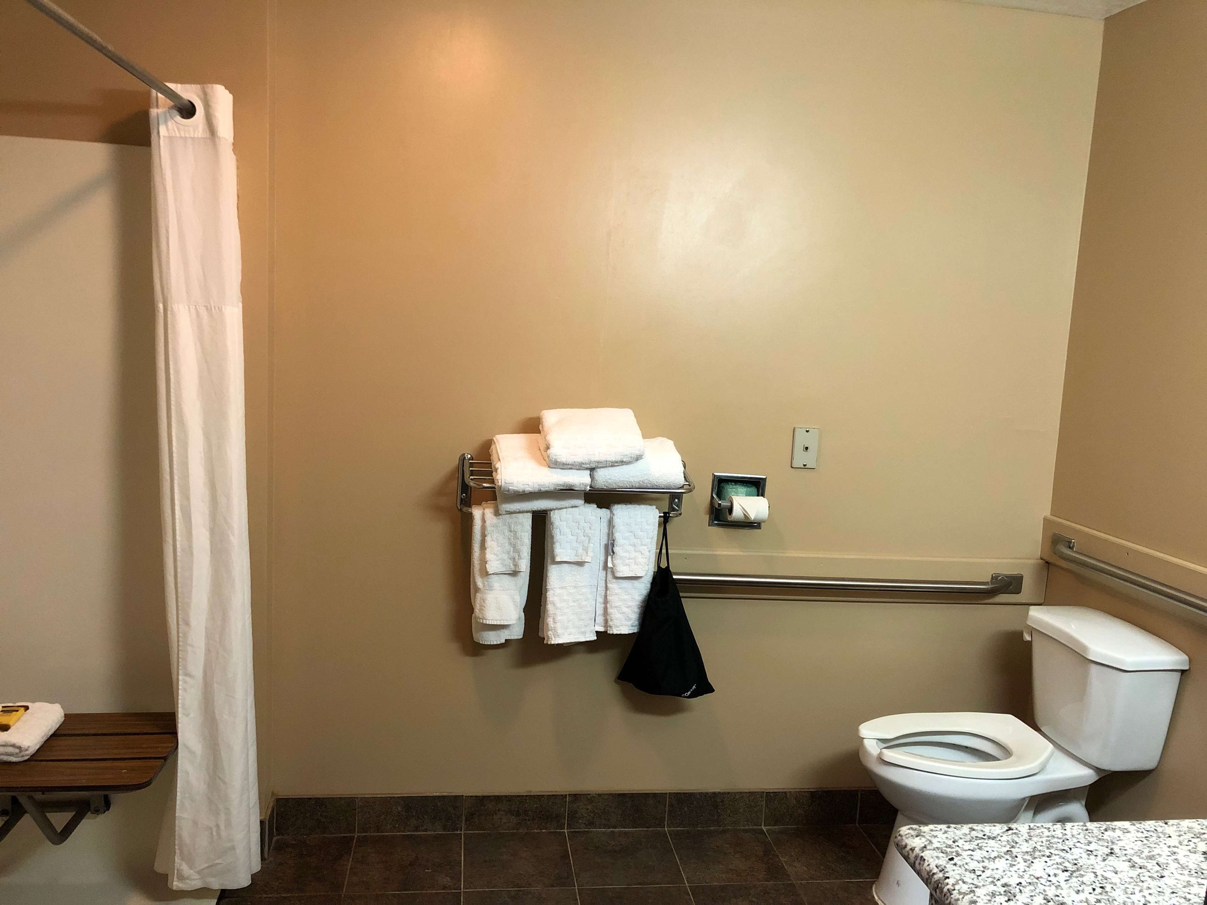 Een badkamer met douchegordijn, een handdoekrek met opgevouwen handdoeken, een toilet en een klein tafeltje met een handdoek.