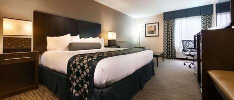 A hotel room with a large bed, a desk, a chair, a TV, and a window with curtains.
