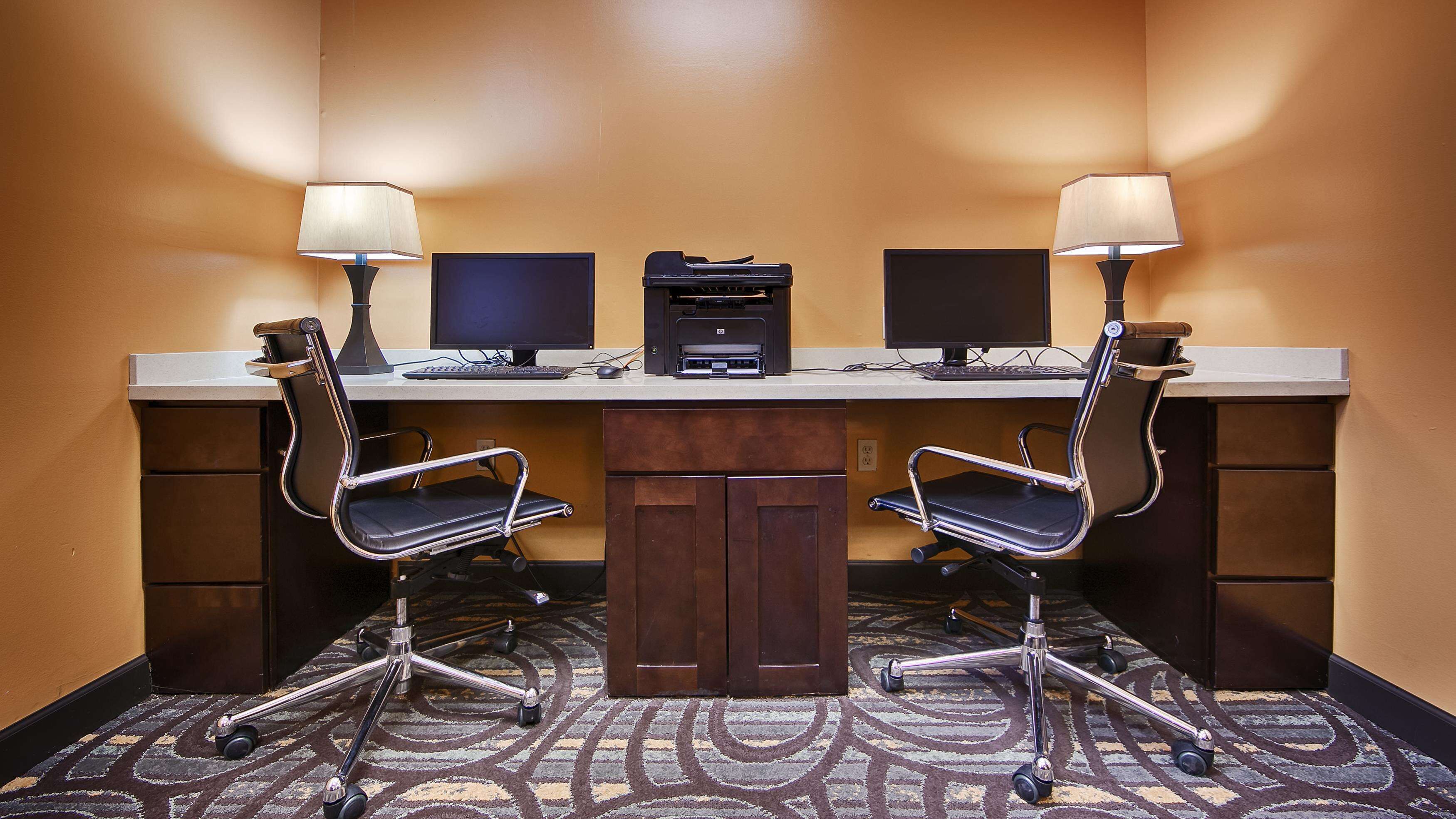 Una sala de conferencias con dos escritorios, cada uno con monitor de computadora, teclado e impresora. Hay dos sillas de oficina con ruedas y piso alfombrado.
