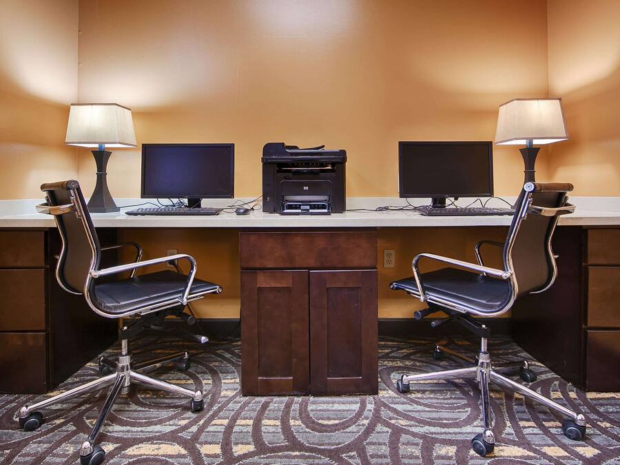 Una sala de conferencias con dos escritorios, cada uno con monitor de computadora, teclado e impresora. Hay dos sillas de oficina con ruedas y piso alfombrado.
