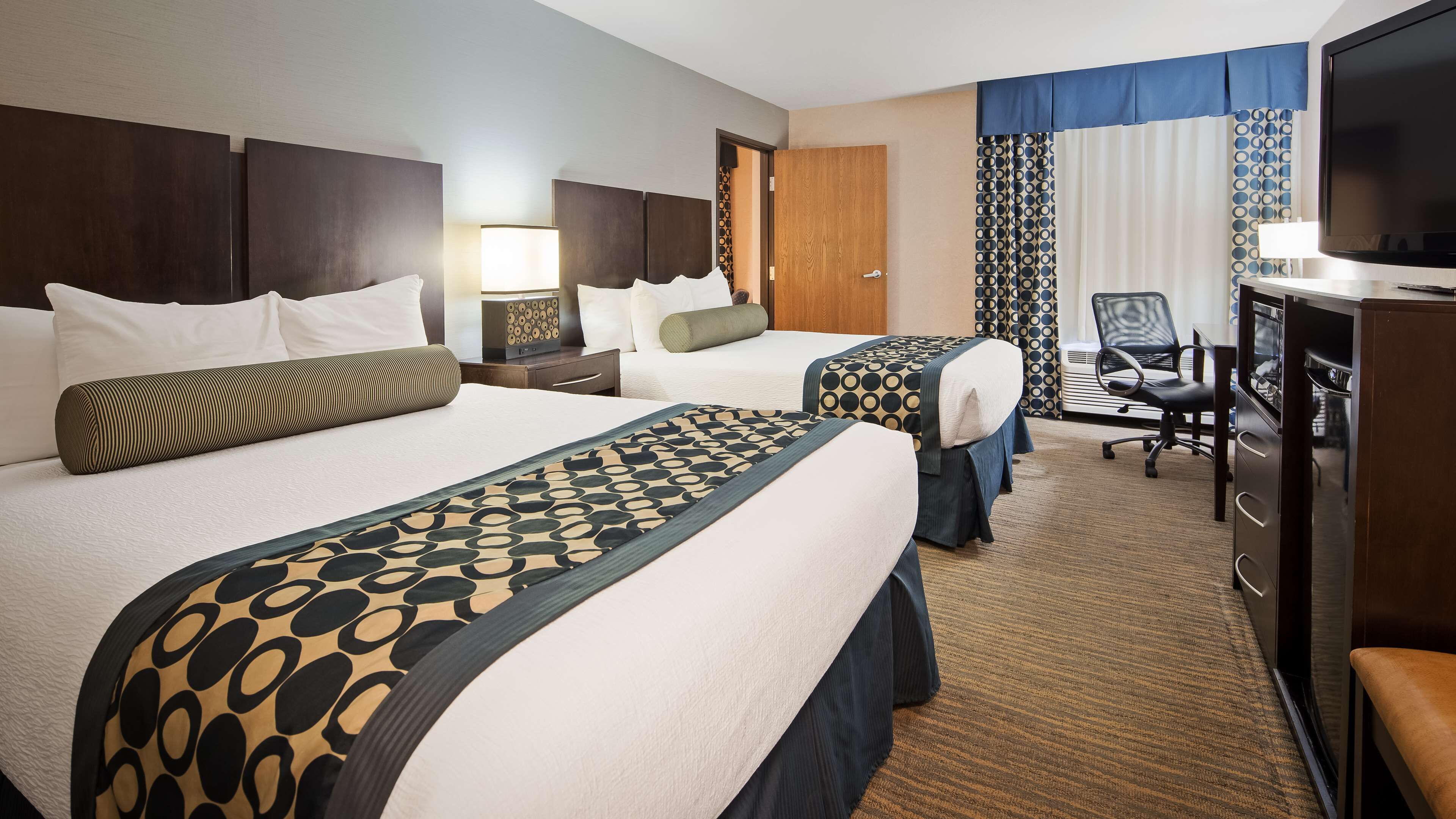 A hotel room with two beds, a desk, a chair, and a television.