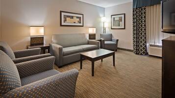 A hotel room with a sofa, armchairs, a coffee table, two lamps, and a television.